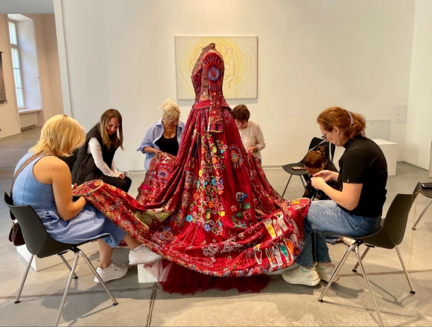 red dress being sewn and stitched on by many women