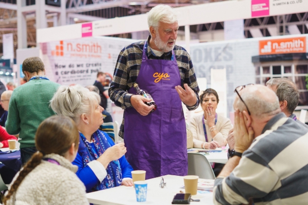 man in purple apron talking to group of people